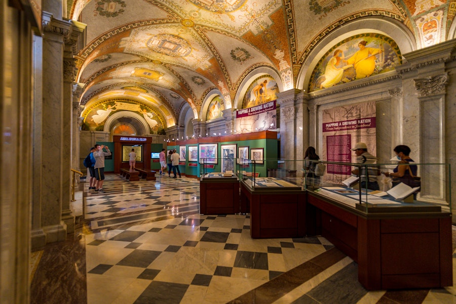 Visitors explore the “Mapping a Growing Nation” exhibit under a vaulted ceiling decorated with murals and gold accents.
