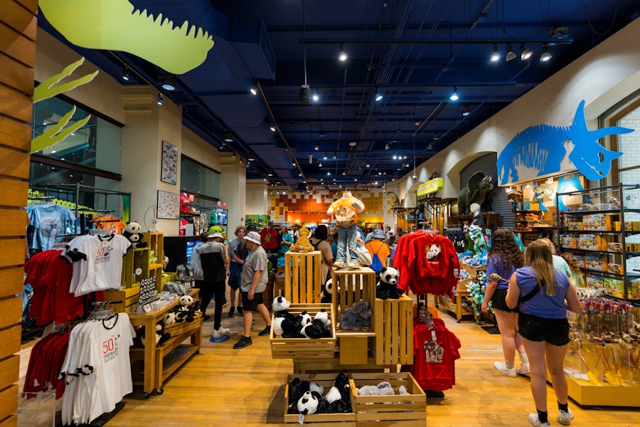 Shoppers browse a colorful museum gift shop filled with plush animals, apparel and dinosaur-themed displays.