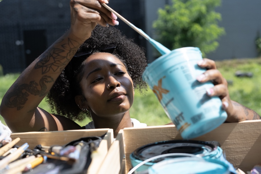 An artist dips a brush into a container of brightly colored paint. 