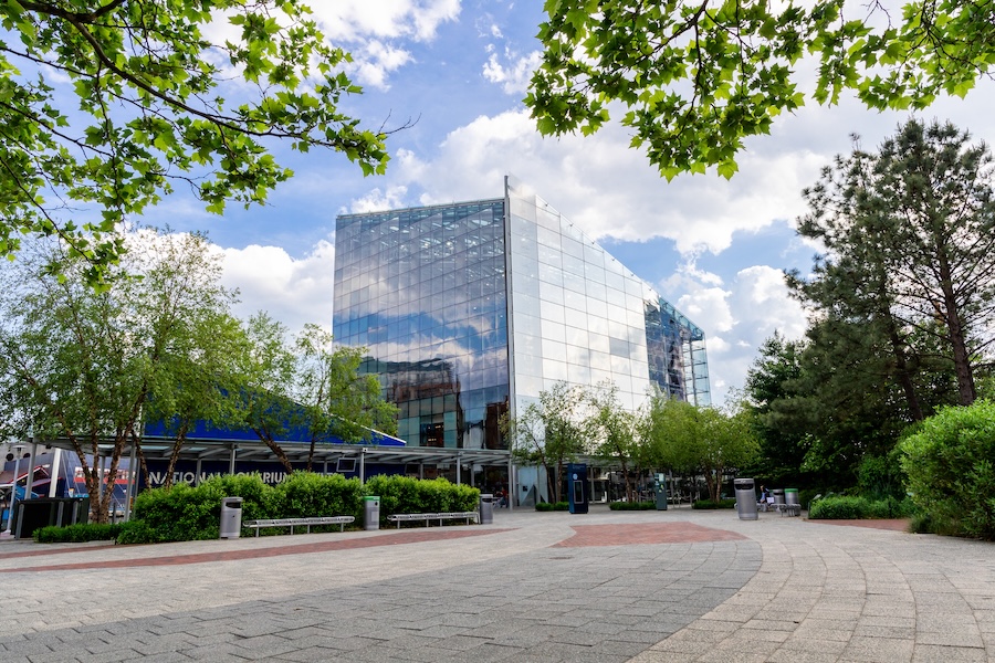 A view of the glass-front National Aquarium building surrounded by trees and greenery under a partly cloudy sky in Washington, DC.