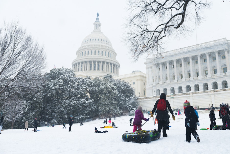 Families and children sled down a snowy hill in front of the U.S. Capitol during a winter day in Washington, DC.