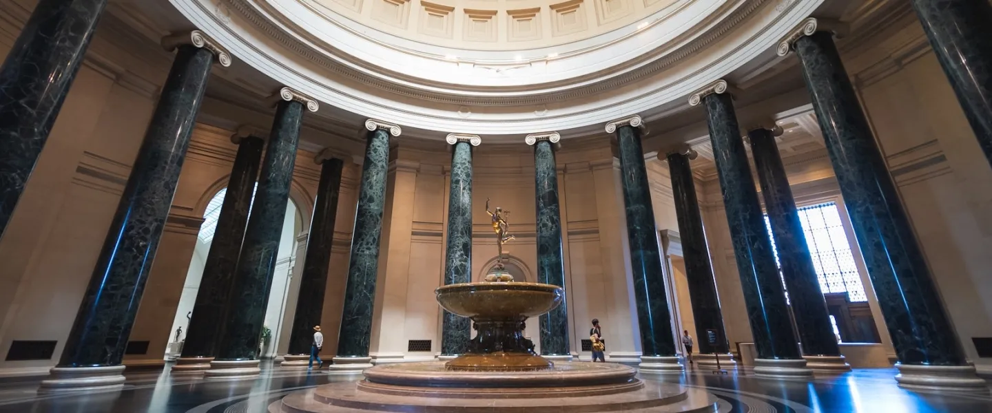 Grand rotunda of the National Gallery of Art featuring a circular fountain and towering marble columns.
