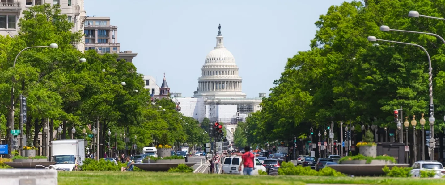A wide view of Pennsylvania Avenue, lined by trees and leading toward the U.S. Capitol Building.