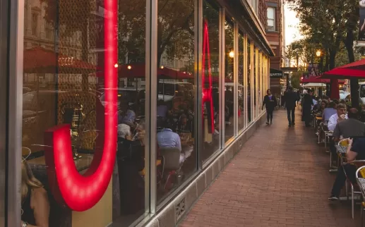The exterior of Jaleo by José Andrés in Washington, DC, with large red neon lettering and outdoor seating under red umbrellas.