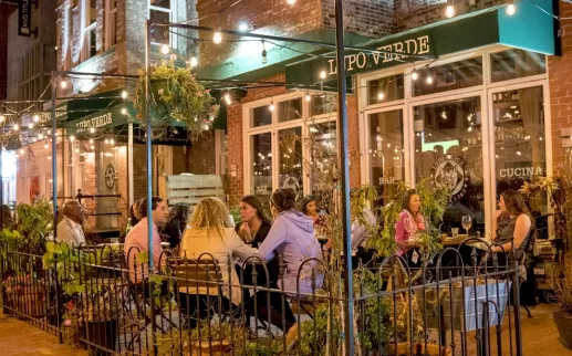Diners enjoy a cozy evening meal under string lights on the outdoor patio of Lupo Verde along 14th Street.
