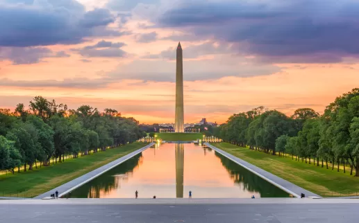The Washington Monument glows at sunset with a colorful sky reflected in the Lincoln Memorial Reflecting Pool in Washington, DC.
