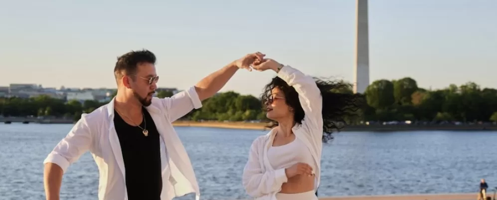 Two people dance with the Washington Monument in the background. 