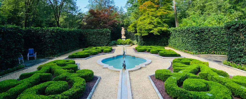 Formal garden with sculpted boxwood hedges, a central fountain, and a classical statue surrounded by tall green hedges in Washington, DC.