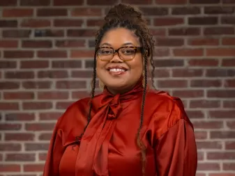 A woman in a red blouse and glasses smiles for a professional headshot. 